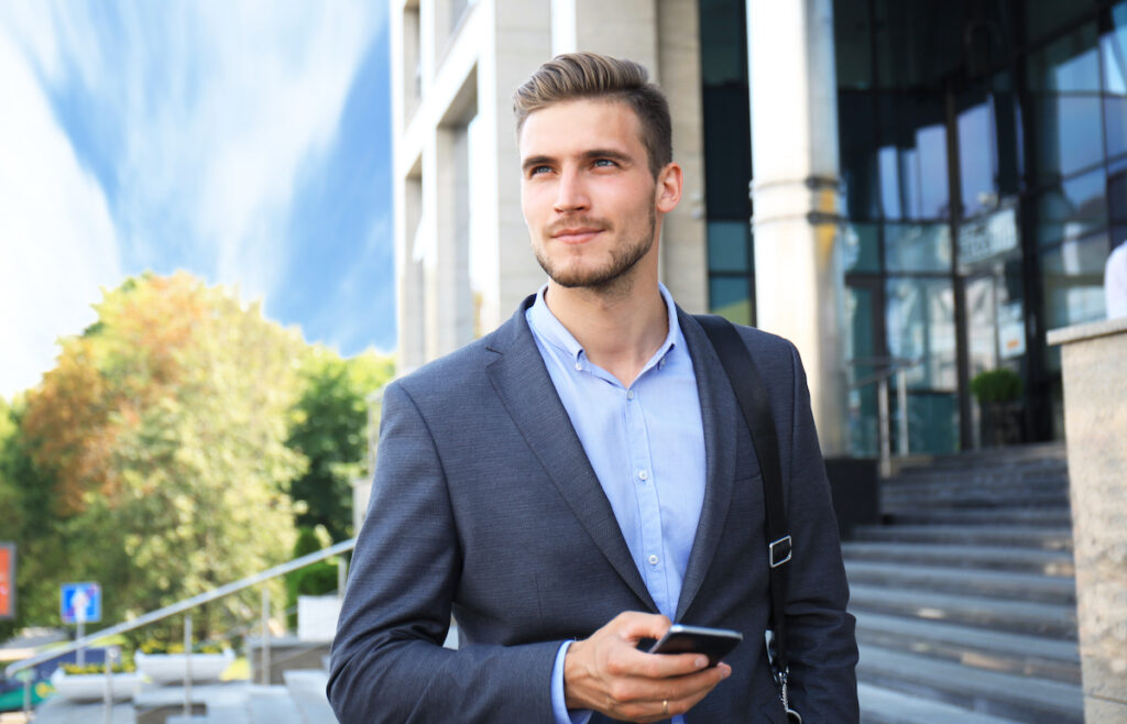 young businessman walking downtown holding a smartphone